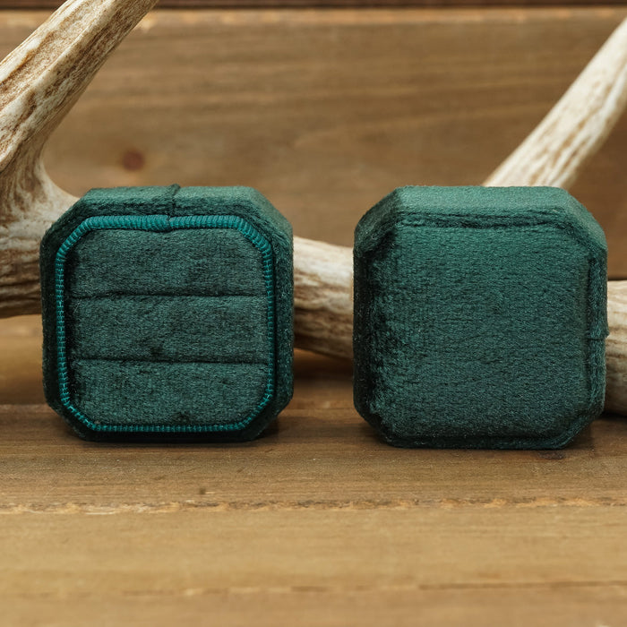 Two 2 Slot Velvet Ring Boxes in green—one open to display rings and one closed—are arranged on a wooden surface with a deer antler in the background, making them perfect for adding rustic elegance to proposal photo shoots or wedding photography.