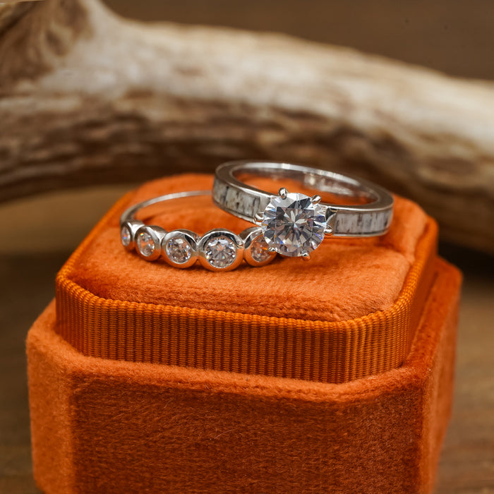 Two silver rings with diamonds rest in a 2 Slot Velvet Ring Box in vivid orange—an elegant touch often seen in wedding photography. One ring showcases a large center diamond flanked by smaller side stones, while the other displays a distinctive patterned band.