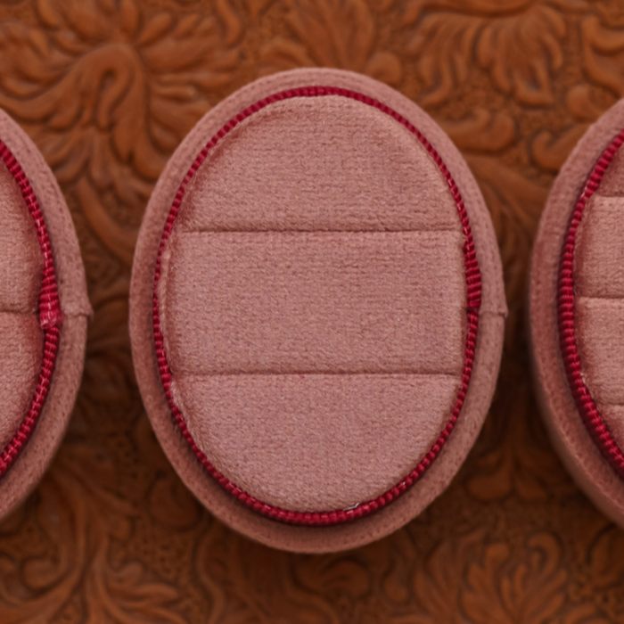 A close-up of the 2 Slot Velvet Ring Box - Promo* in pink velvet with red trim, displayed on an embossed brown surface. Ideal for proposal photo shoots or wedding photography, the box features an empty interior.