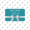 Teal Antler Ring E-Gift Card featuring a white bow and labeled with "Antler Rings: A Wildlife Design Co. Gift Card." The background displays a repeating gray deer silhouette pattern, making it the ideal gift for anyone who appreciates unique antler ring designs from AntlerRings.com.