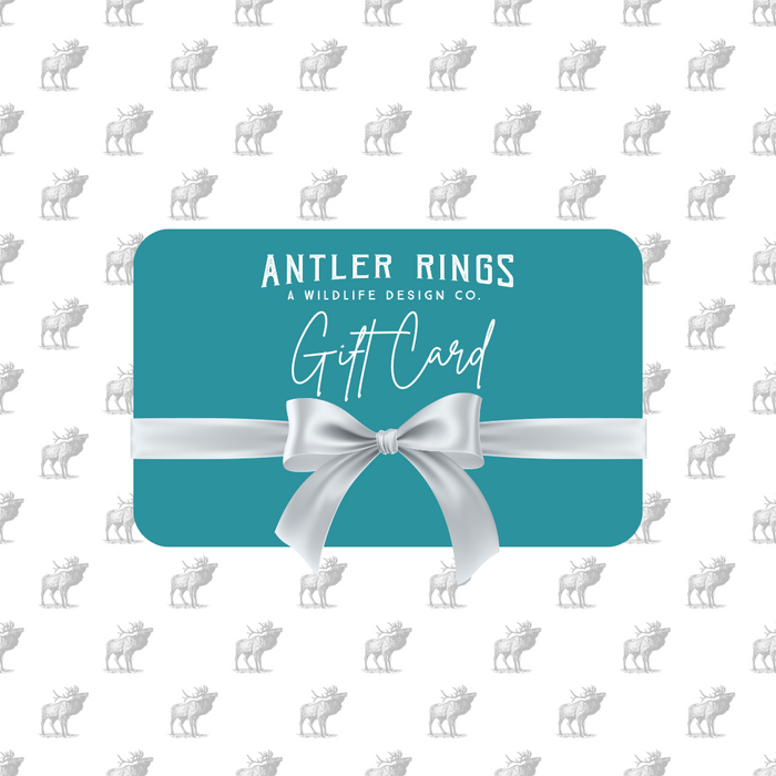 Teal Antler Ring E-Gift Card featuring a white bow and labeled with "Antler Rings: A Wildlife Design Co. Gift Card." The background displays a repeating gray deer silhouette pattern, making it the ideal gift for anyone who appreciates unique antler ring designs from AntlerRings.com.