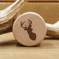 A round beech wood Antler Ring Gift Box with a silhouette of a deer head and antlers engraved on it, placed in front of a large antler on a wooden surface, reminiscent of an elegant display for an antler ring.