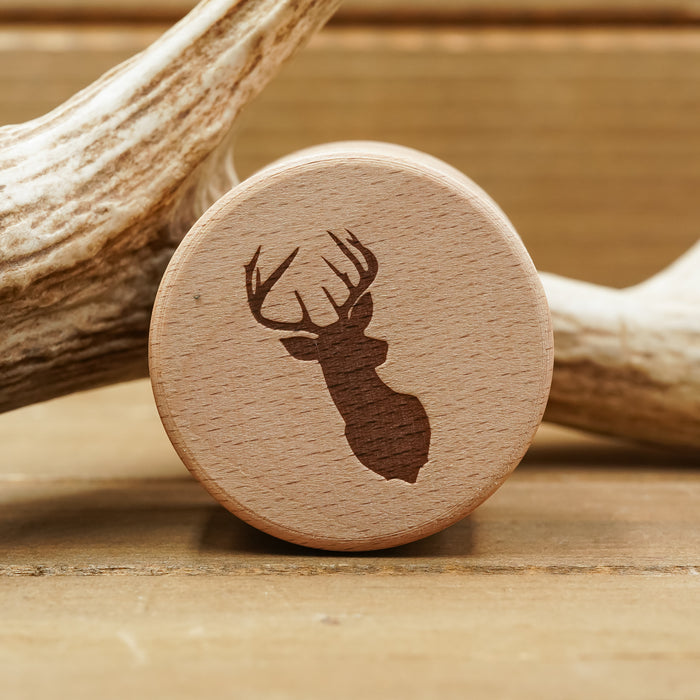 A round beech wood Antler Ring Gift Box with a silhouette of a deer head and antlers engraved on it, placed in front of a large antler on a wooden surface, reminiscent of an elegant display for an antler ring.