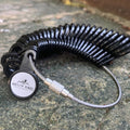 A set of AntlerRings Ring Sizer—black rings secured by a metal cable—rests on a textured stone surface outdoors, providing an easy and accurate way to measure your ring size with this convenient tool.