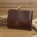 A Deer Leather Wallet featuring a moose and mountain design rests on a wooden surface, propped against antlers—a perfect outdoorsman accessory that blends rustic charm with practicality.
