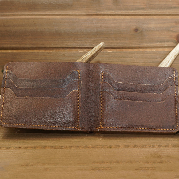 A handmade Deer Leather Wallet in rich brown, featuring visible card slots, rests on a wooden surface—making it the ideal accessory for any outdoorsman.
