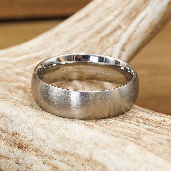 A minimalist women's Stainless Steel Wedding Band—featuring a polished finish with a subtle brushed texture—rests on a light-colored antler.