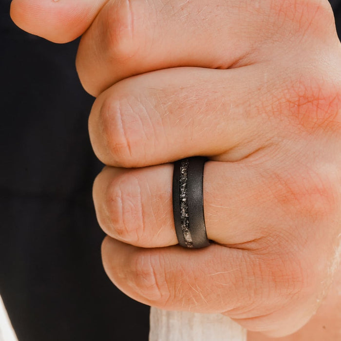 A close-up of a hand gripping a white rope, wearing The Allende—a matte black tungsten carbide ring featuring a textured, stone-like inlay reminiscent of meteorite—on the ring finger.