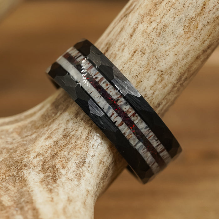 The Benton is a black tungsten carbide ring with a faceted surface, showcasing a central inlay of red and white and set against a textured antler background.