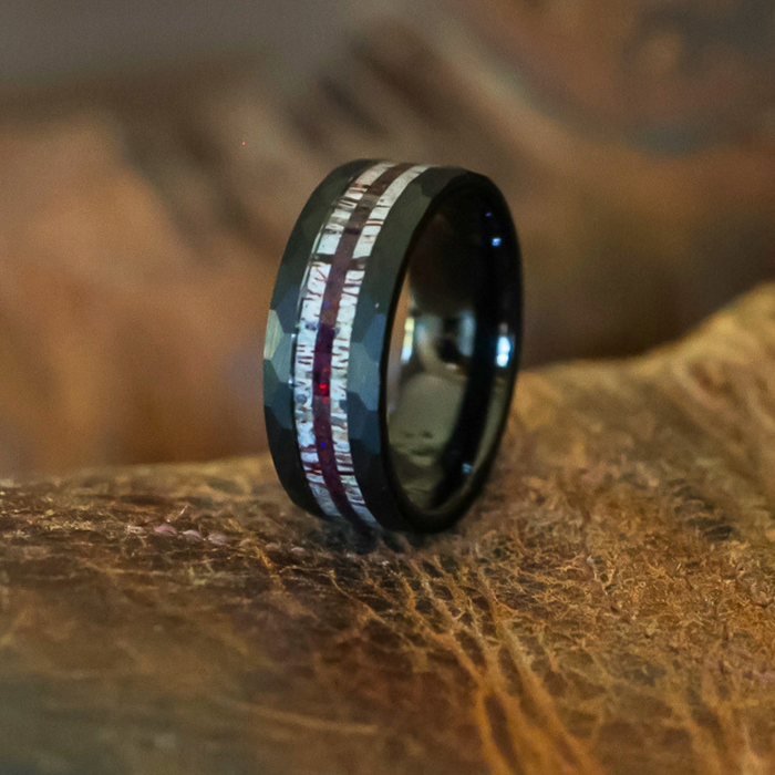 The Benton, a black tungsten carbide ring featuring two metallic, iridescent inlays, rests on a textured brown surface.