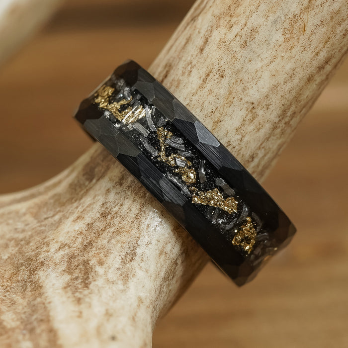 The Brenham is a black hammered ring featuring embedded gold and silver flakes, showcased on a light brown antler.