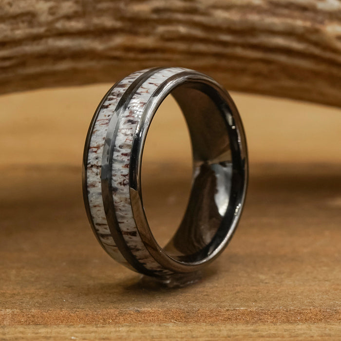 The Bryce Canyon is a black Tungsten Carbide ring featuring a wide inlay of textured, white material with brown speckles reminiscent of natural antler, showcased on a wooden surface with a softly blurred wooden background.