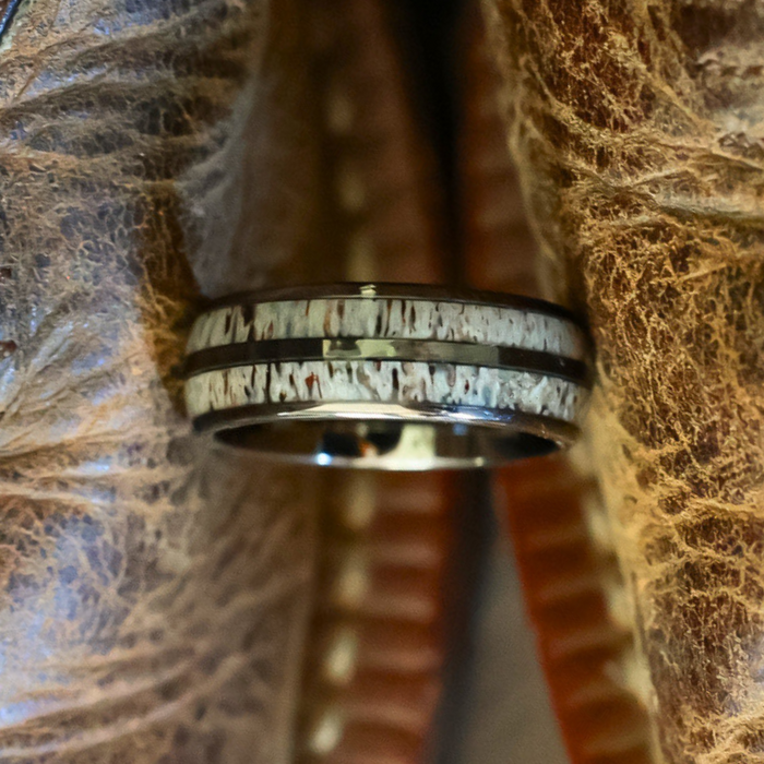 A close-up of The Bryce Canyon, a Tungsten Carbide ring featuring a textured white inlay and dark edges, positioned vertically between two pieces of worn brown leather.