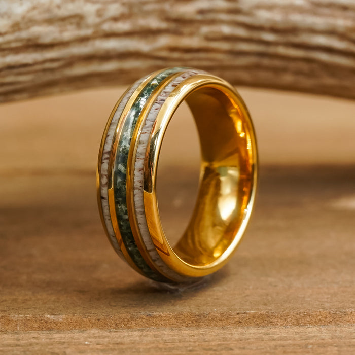 The Butano, a gold Tungsten carbide ring featuring two inlaid bands—one green and one beige—stands upright on a wooden surface with a softly blurred wood background.