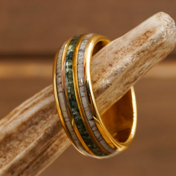 Resting on a textured, beige antler, The Butano is a gold antler ring featuring two stone inlays—one vibrant green moss agate and one speckled white.