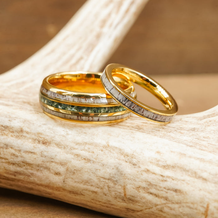 Two gold rings, including The Butano, rest on a light-colored antler. The larger ring—The Butano—is a striking tungsten carbide band with inlaid green and silver bands reminiscent of green moss agate, while the smaller ring features a textured silver inlay. Both rings have shiny finishes and intricate detailing.