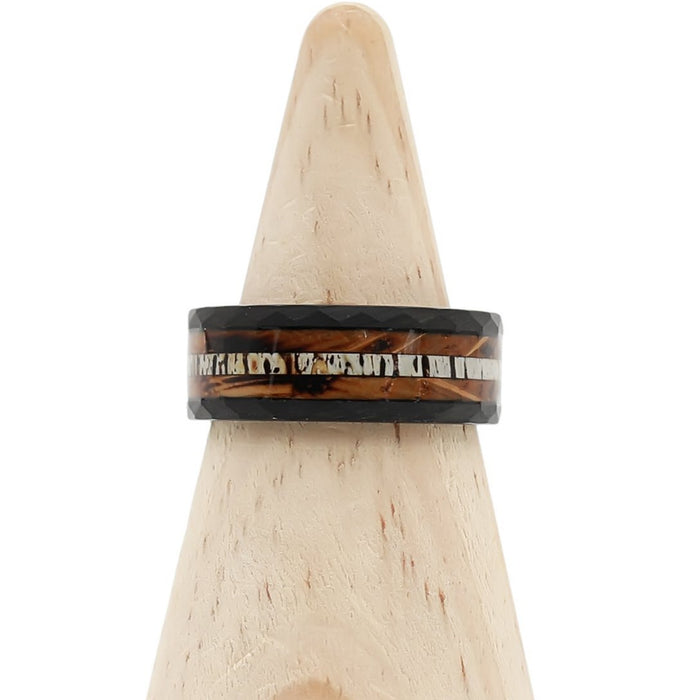The Custer, a black hammered tungsten ring featuring brown and silver inlays, is displayed on a light wooden cone stand and shown from the front.