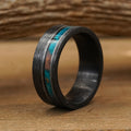 The Eagle Canyon ring, crafted from durable Tungsten Carbide with an 8mm width, showcases a striking black brushed finish and a turquoise and brown inlay stripe. It stands upright on a wooden surface, set against a softly blurred wood background—blending modern elegance with rugged resilience.
