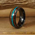 The El Capitan, a black tungsten carbide ring featuring a shiny turquoise inlay and a wooden stripe, sits on a wooden surface against a blurred wood-grain background.