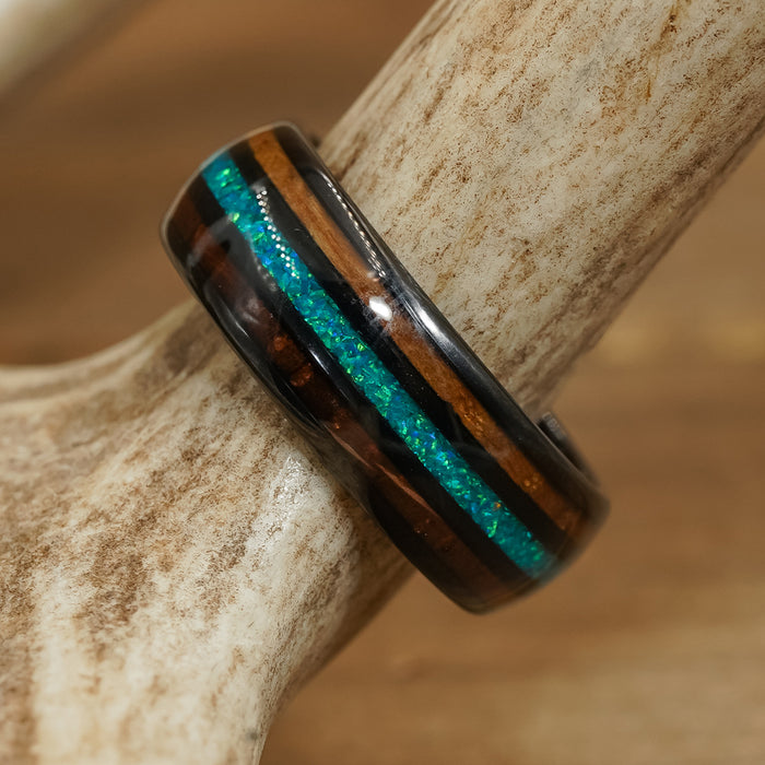 The El Capitan, a whiskey barrel ring featuring dark wood and turquoise blue inlay bands, is displayed on a light-colored antler against a softly blurred brown background.