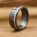 A close-up of The Folsom Lake ring showcases its metallic band with inlays of turquoise, wood, and a light-colored textured material, as it rests elegantly on a wooden surface.