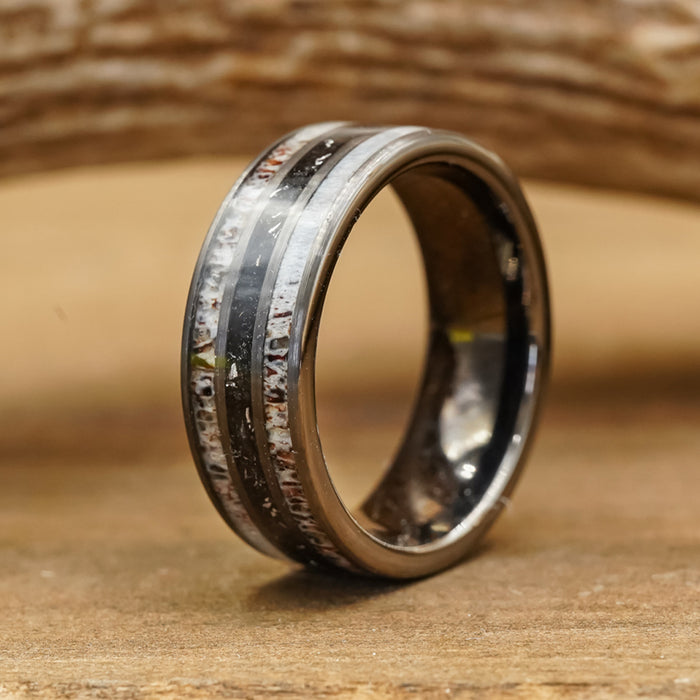 A close-up of The Fossil Ridge, a tungsten carbide ring featuring a weathered, textured inlay, resting on a wooden surface with blurred wood grain in the background.