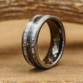 A close-up of The Fossil Ridge, a tungsten carbide ring featuring a weathered, textured inlay, resting on a wooden surface with blurred wood grain in the background.
