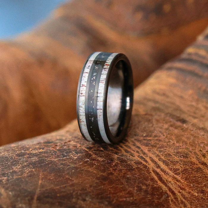 A close-up of The Fossil Ridge ring, featuring two silver-colored bands and a dark center, displayed upright on textured brown leather.