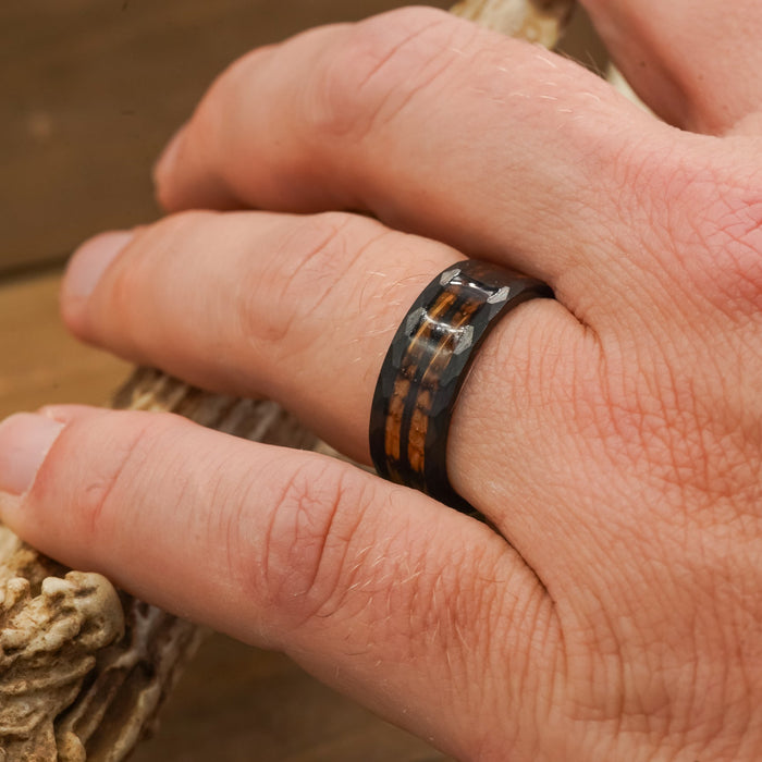 A close-up of a hand wearing The Gatlinburg ring, featuring a brown wood whiskey barrel inlay, while holding a textured light-colored object.