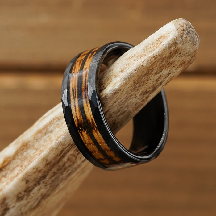The Gatlinburg, a tungsten carbide ring featuring a faceted surface and brown woodgrain inlay, rests on a white antler against a softly blurred wooden background.