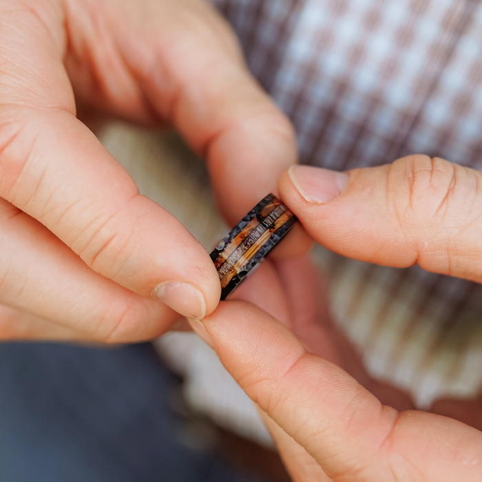 A person wearing a plaid shirt holds The Gifford, a striking antler ring crafted from wood and stone, with both hands. Visible layers and patterns accentuate its unique design.