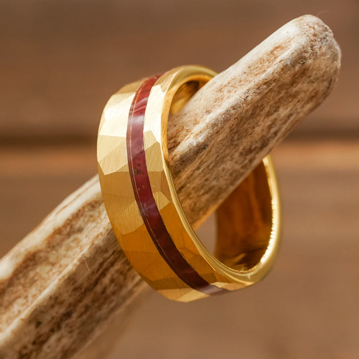 The Golden Canyon ring, featuring a faceted texture and a reddish-brown inlay, is displayed resting on light-colored wood, emphasizing the distinctive style of this gold-plated hammered piece.