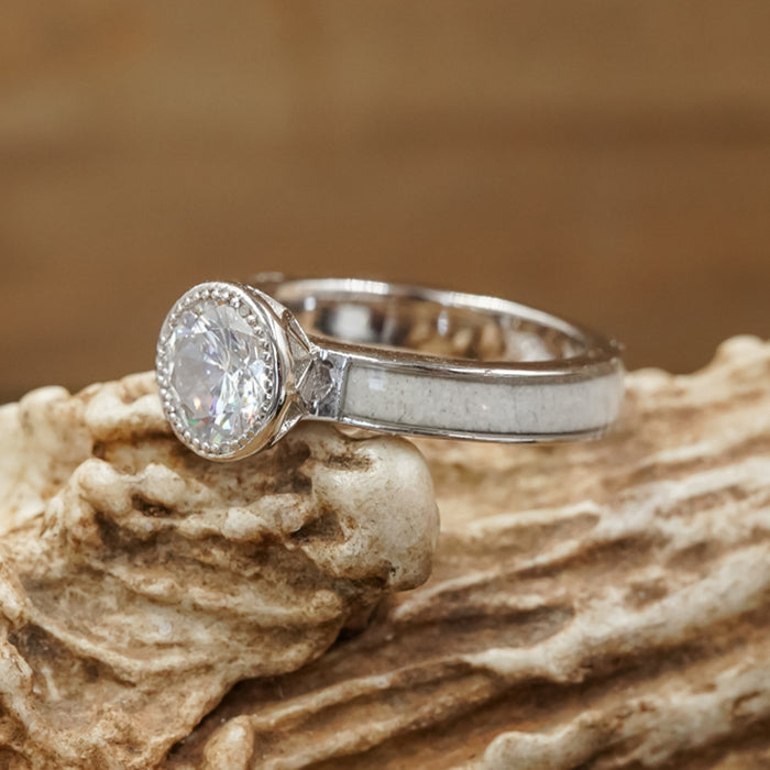 A striking engagement ring named The Grand Avonelle, crafted with a white antler inlay, showcased on a textured, light brown stone background.