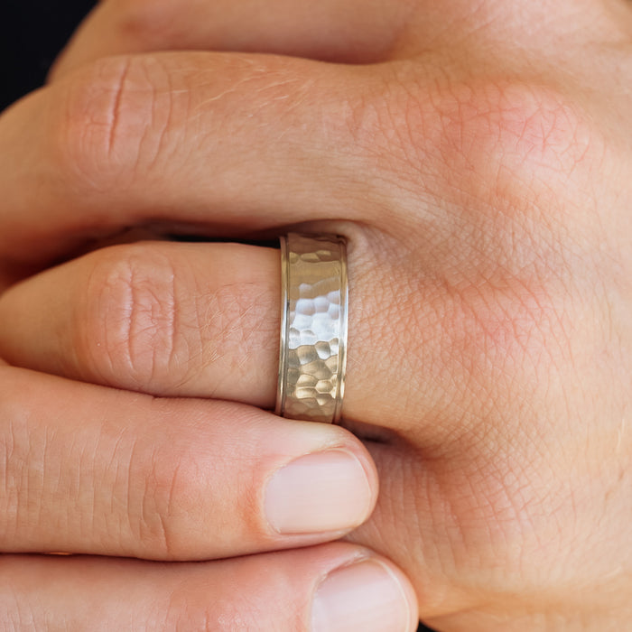 A close-up of a hand wearing The Koa men's wedding band on the ring finger, showcasing natural skin texture and visible fingernails.