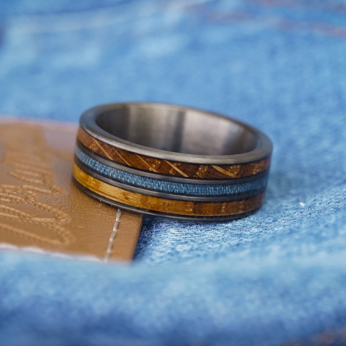 The Lane, a tungsten carbide ring featuring wood and blue inlay, rests on tan leather with a backdrop of blue denim fabric.