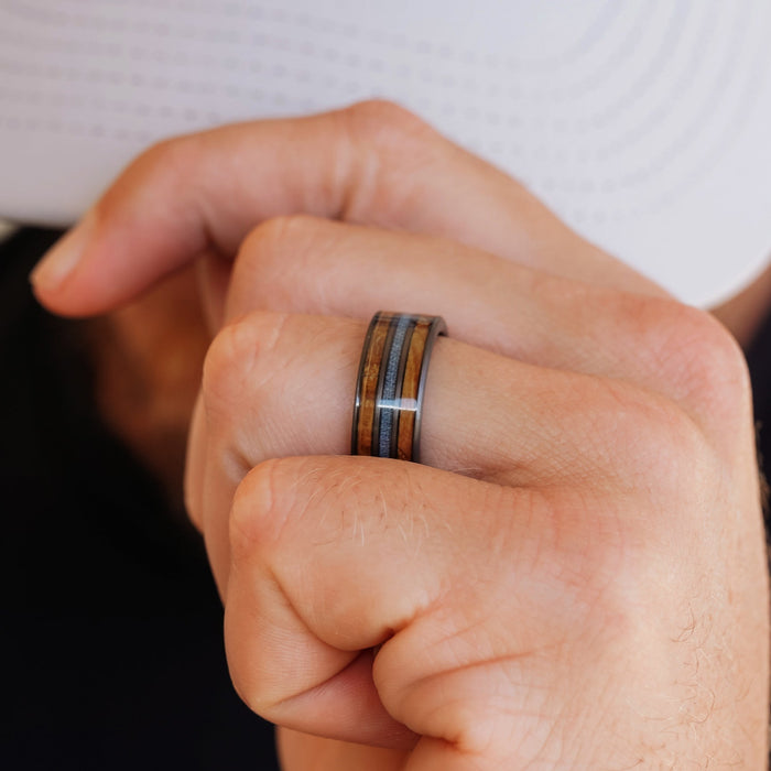 A close-up of a hand wearing The Lane men's band, featuring wood and metal inlays, while holding the brim of a white hat.
