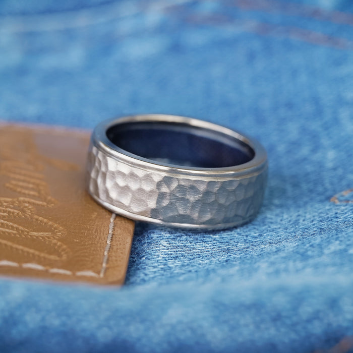 A silver hammered metal ring sits atop a brown leather patch that is stitched onto The Larry's blue denim band.