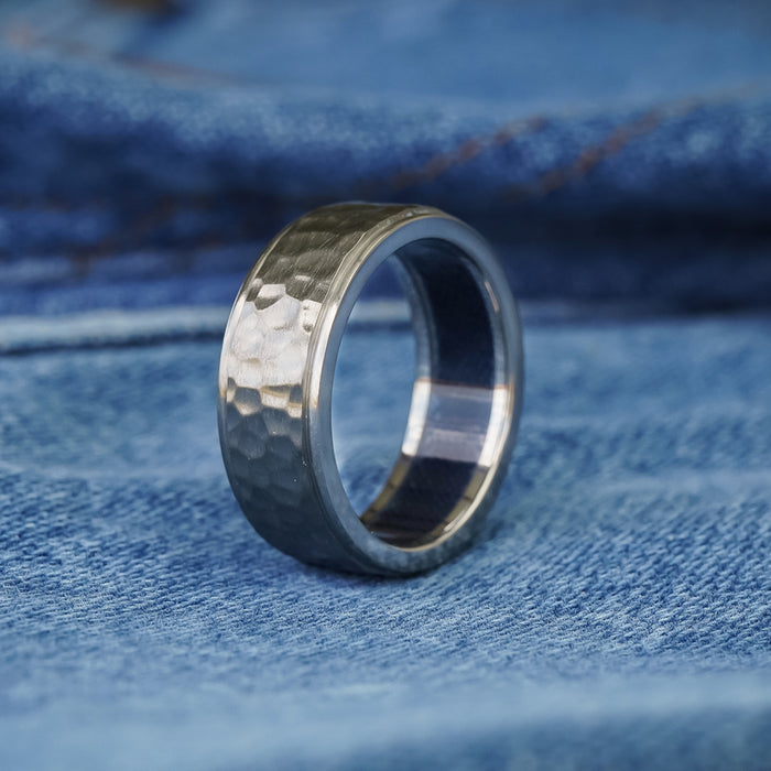 The Larry, a hammered titanium ring with a matte finish, is displayed upright on blue denim fabric, highlighting the visible texture and stitching in the background.