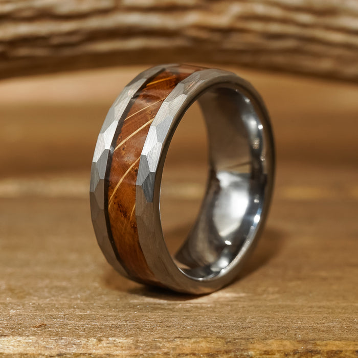 The Lawrenceburg, a silver tungsten carbide ring with a faceted edge, featuring a wood inlay and a thin gold stripe, rests elegantly on a wooden surface.