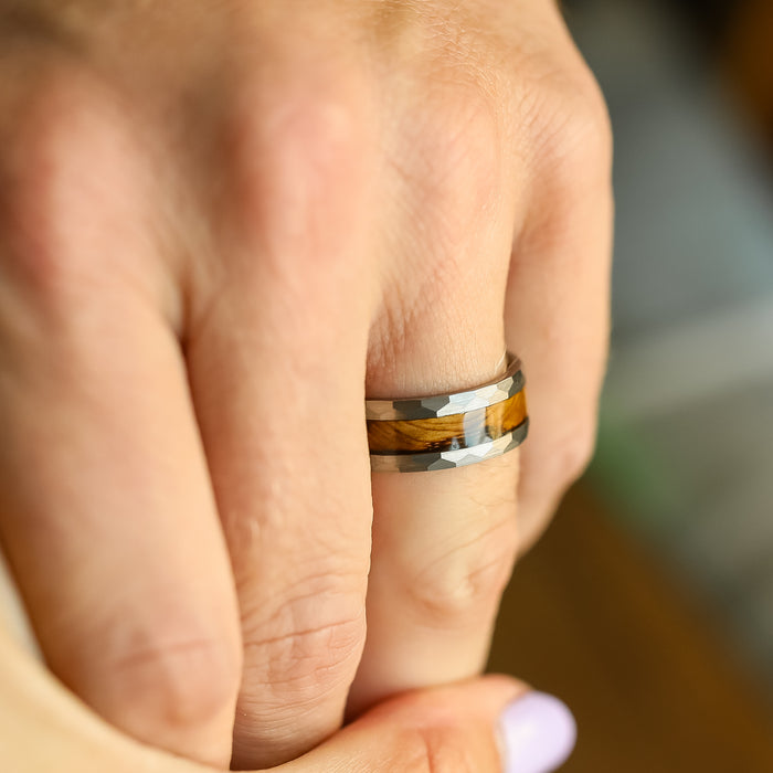 A close-up of a hand wearing The Lawrenceburg, a hammered men’s wedding band with a brown and gray camouflage pattern, holding another person’s hand.