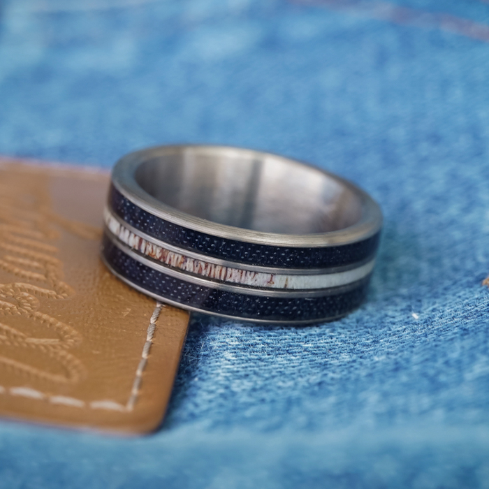Introducing The Leon: a stylish men’s band, this silver ring featuring black and white inlay is displayed on a tan leather patch against classic blue denim fabric.