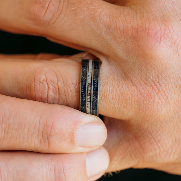 A close-up of a hand wearing The Leon antler ring, showcasing its unique design with contrasting dark and light-colored inlays, gently held by the other hand.