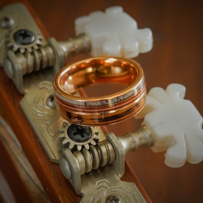 The Letchworth ring in rose gold rests on the tuning pegs of a vintage string instrument adorned with white knobs and ornate metal gears.