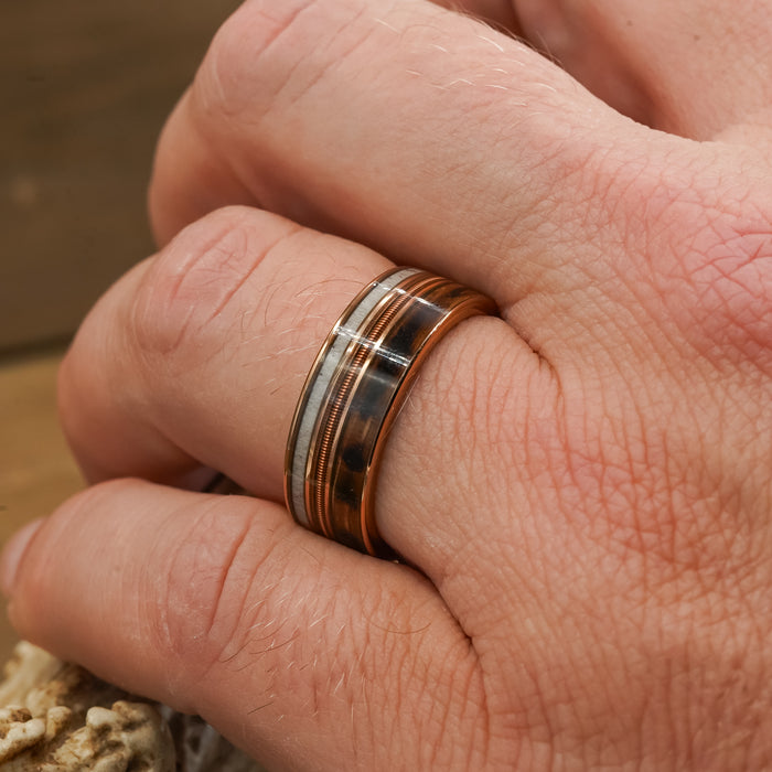 A close-up of a hand wearing The Letchworth, a multi-colored tungsten carbide ring with metallic and brown bands, featuring a polished finish.