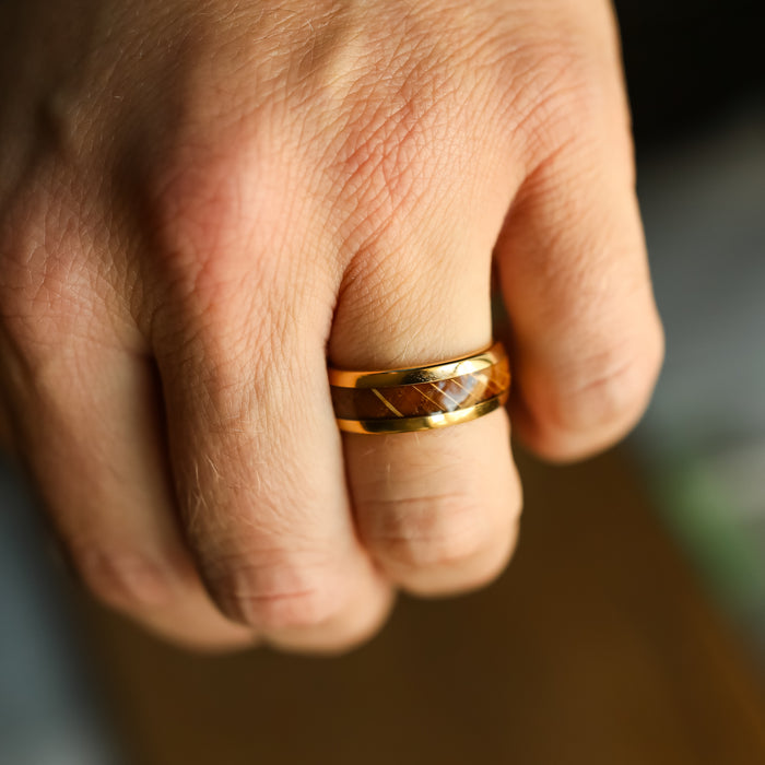 A close-up of a hand wearing The Loretto, a shiny gold tungsten men's wedding band featuring a striking marbled pattern, highlighting the skin's texture and the intricate details of the ring.