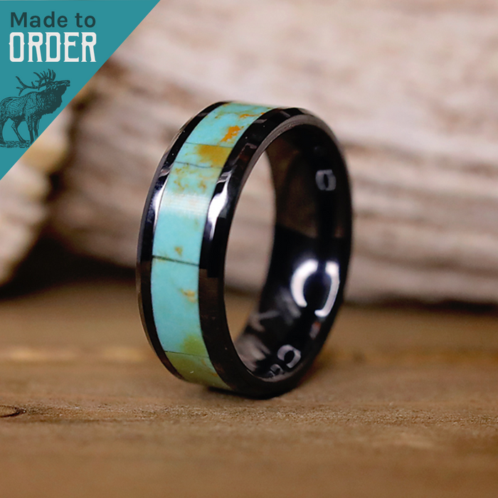 Introducing The Los Glaciares: a distinctive men’s black ceramic ring with a bold turquoise and brown inlay, showcased standing upright on a wooden surface. A turquoise triangle featuring an elk graphic and the words "Made to Order" appears in the top left corner.