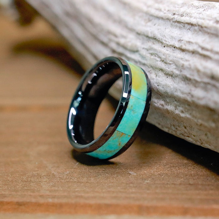 Introducing The Los Glaciares: a unique men's ring crafted from striking black ceramic and accented with a vivid turquoise inlay, showcased upright against driftwood on a wooden surface.