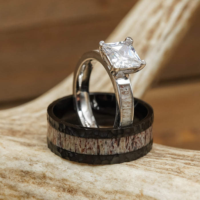 The Lowell, a silver engagement ring featuring a large square diamond set upright within a black and silver textured band reminiscent of a men's hammered ring, is displayed resting on a piece of antler against a wooden background.