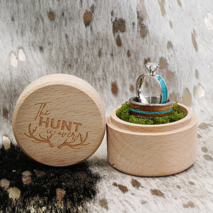 Two "The Mount Vernon" wooden ring boxes, one open to display three rings nestled on moss—among them a turquoise ring with a crushed turquoise inlay and a tungsten carbide ring—while the closed box lid features "The Hunt is Over" and antler graphics, all set against a fur-patterned background.