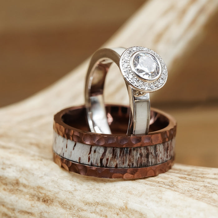 The Mount Vinson, a silver engagement ring with a round diamond and a wide, hammered band featuring copper and white inlay, is displayed on a light wood surface, embodying the rugged elegance often seen in men's wedding bands or distinctive hammered antler rings.